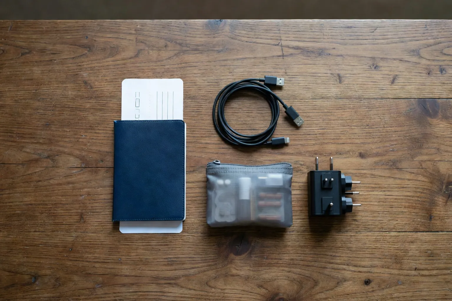 Objets essentiels de voyage disposés à plat : passeport, chargeur, adaptateur